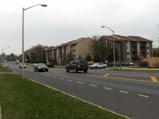 photo shows a street with two lanes going each way plus a middle turning lane.  Nine vehicles are visible on the street and another is about to enter from a parking lot.